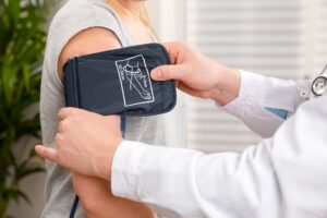 Doctor wrapping a blood pressure cuff around a woman's arm in a clinical setting.