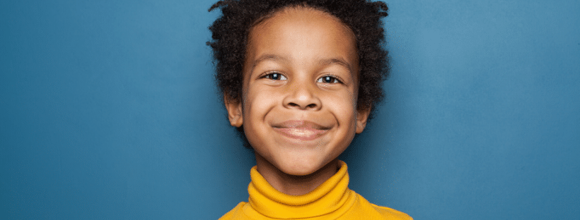 Smiling young African American boy wearing a yellow sweater against a blue background