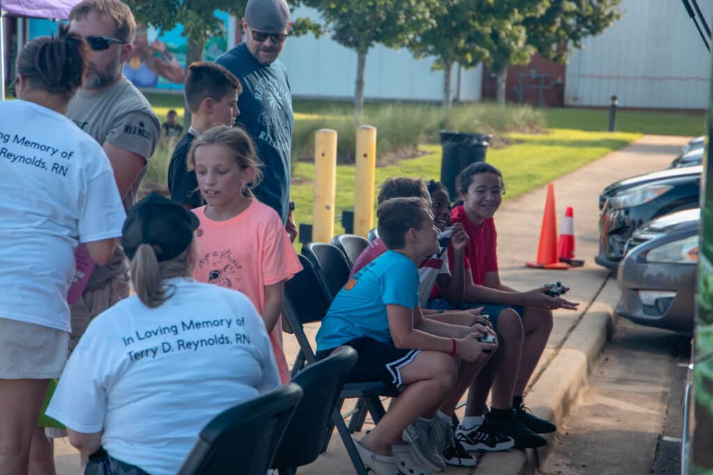 Kids are smiling playing video games on the Zone Mobile Unit Community Fun & Wellness Block Party.